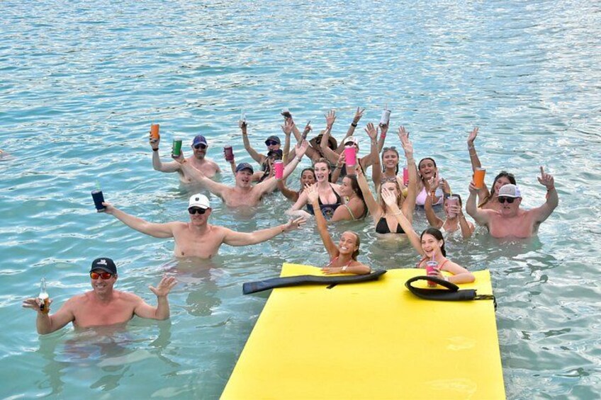 Un groupe de personnes se trouve dans une étendue d’eau. Certaines sont sur un flotteur jaune, tandis que d’autres tiennent des boissons à la main. 2