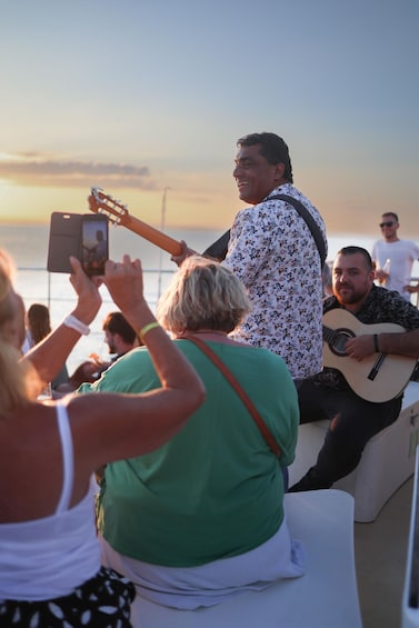 A person playing guitar on a boat with a sunset in the background. 2