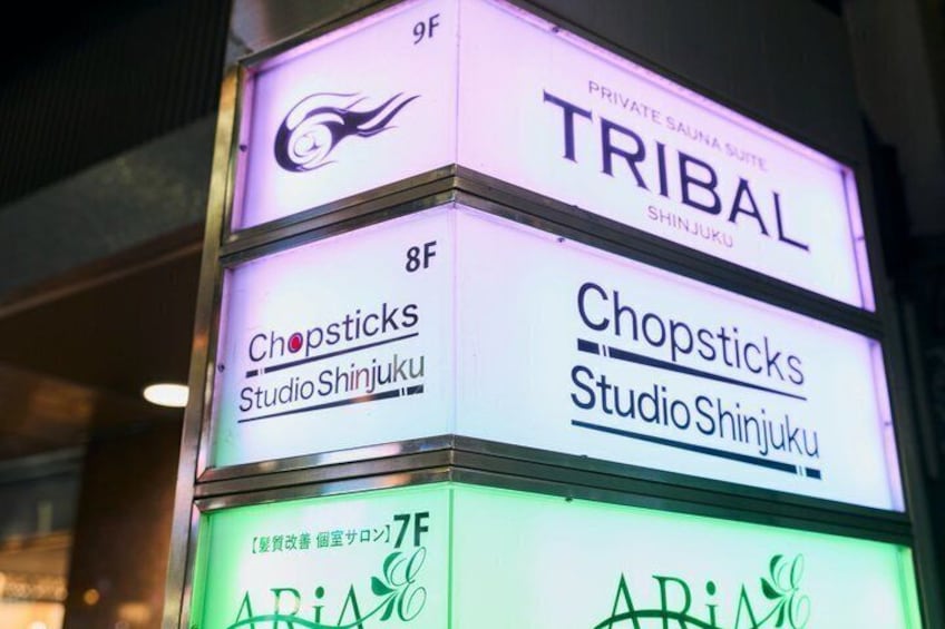 Un edificio de varios pisos con letreros iluminados que dicen 'TRIBAL', 'Chopsticks Studio Shinjuku' y 'ARIA'. 2
