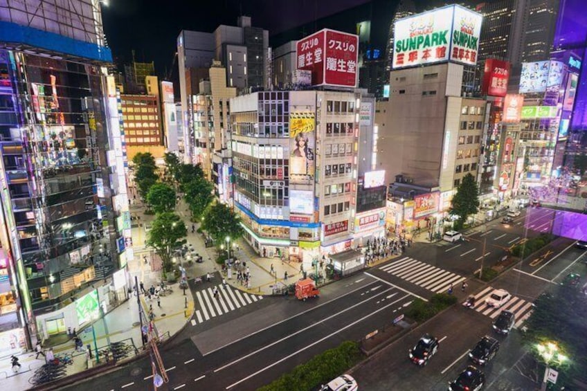 Un paisaje urbano nocturno con edificios iluminados, un paso de peatones y una calle concurrida. 5