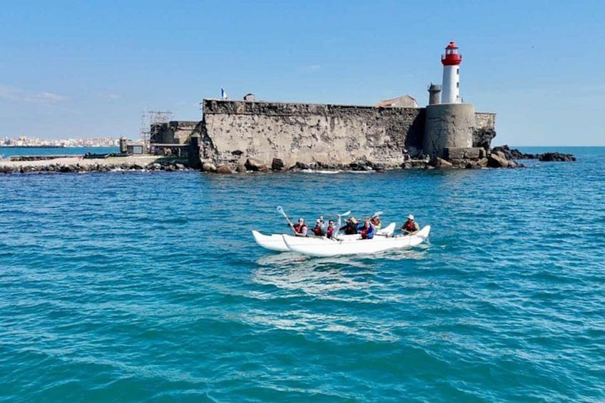 A boat with people on a calm sea, a lighthouse, and a stone wall in the background. 1
