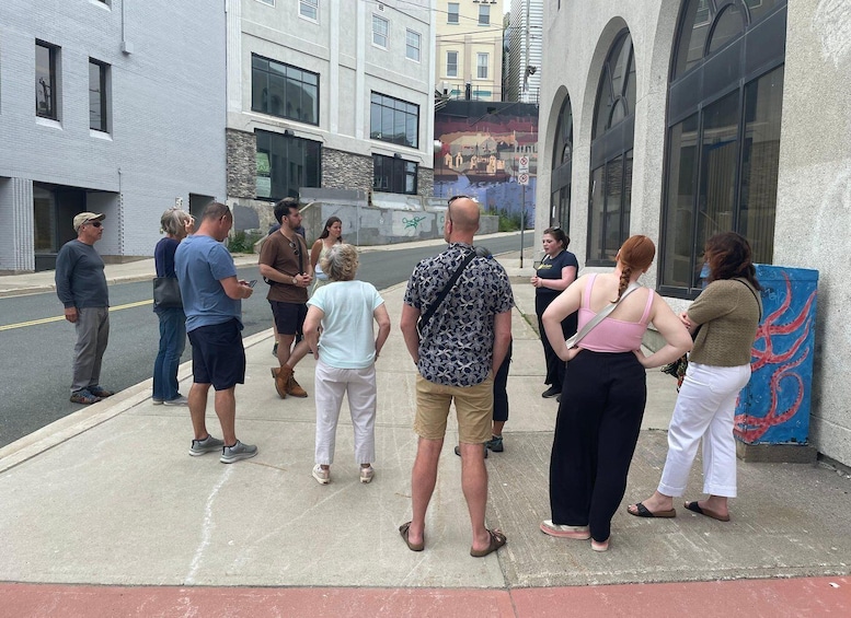 A group of people standing on a sidewalk, facing a mural on a building wall. 3
