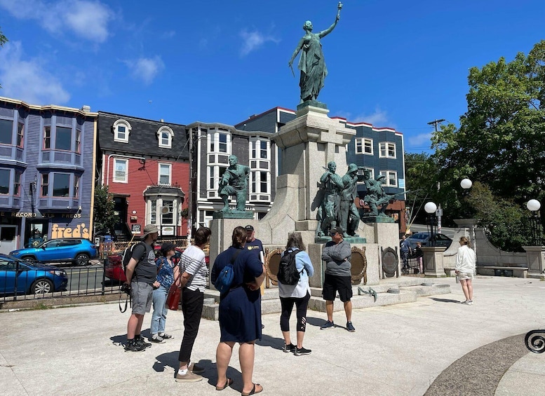 A public square with a statue of a woman holding a torch, surrounded by people. 4