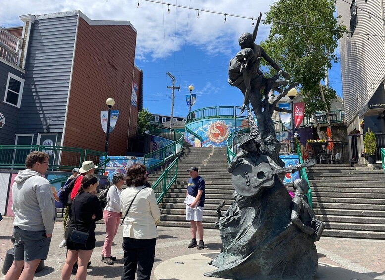 A statue of a man playing a guitar on a fountain, surrounded by people and buildings. 5
