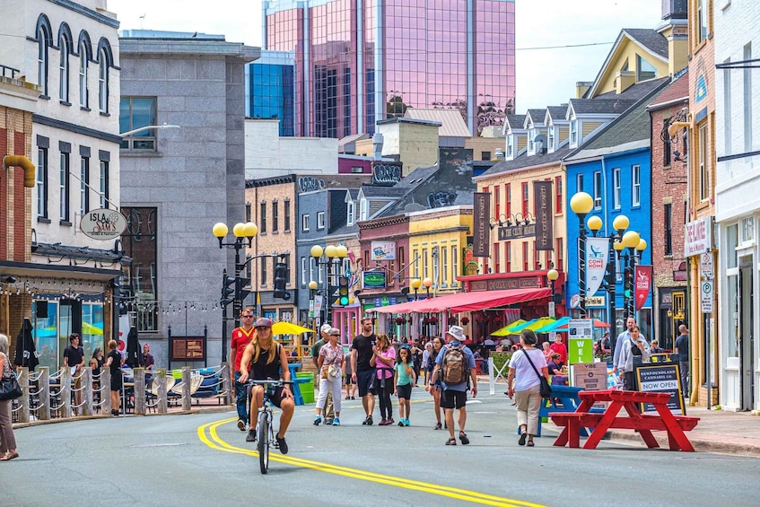 A bustling street with people walking, cycling, and dining in colorful buildings. 1