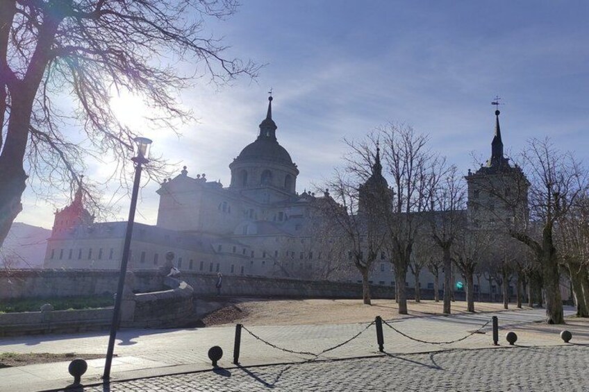 A historic building with domed architecture, a paved area with trees, and a clear sky. 3
