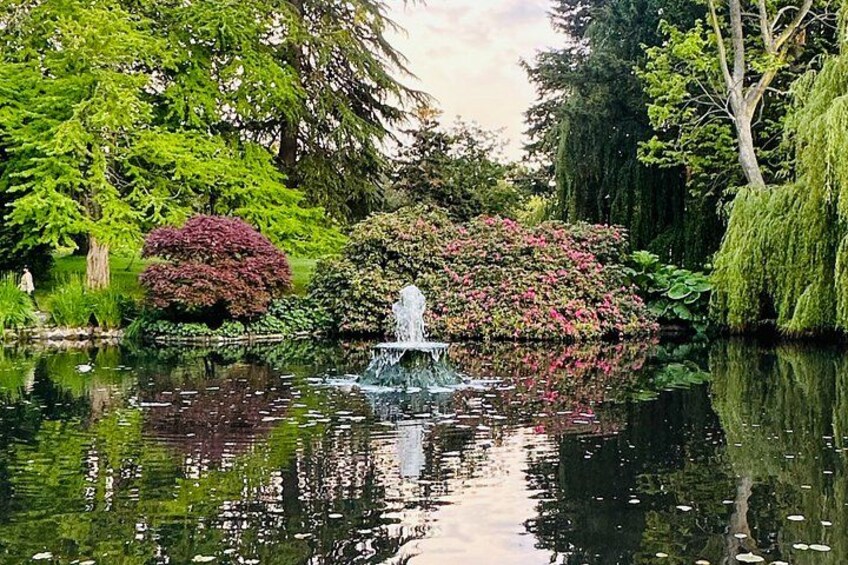 A pond with a fountain, surrounded by lush greenery and flowering bushes. 2