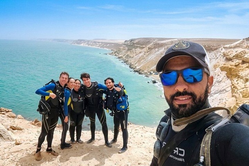 A group of divers on a rocky coastline with clear blue water. 1