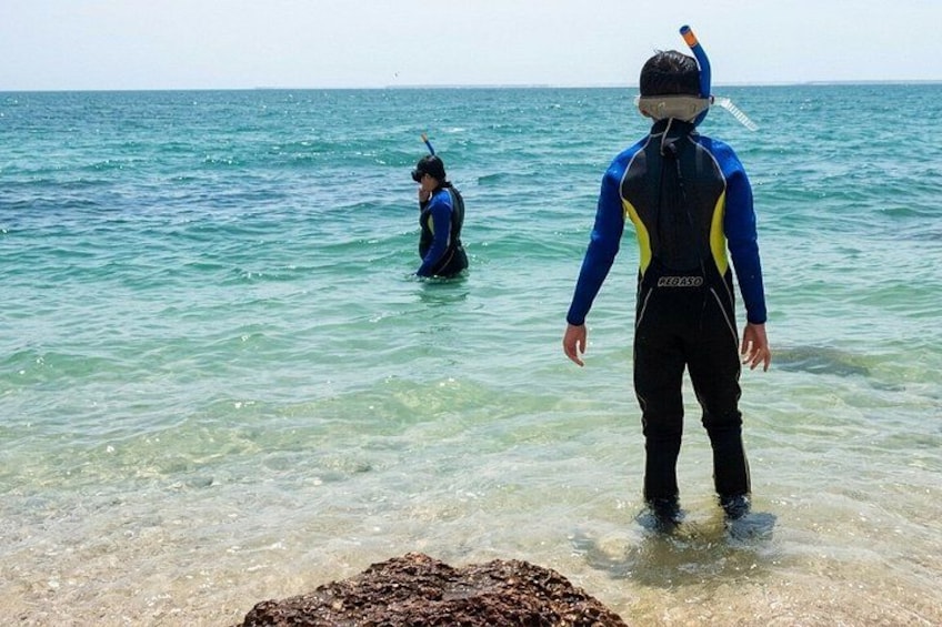 Two people in wetsuits standing in shallow water, one closer to the shore and the other further out. 2