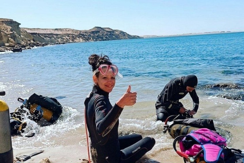 Two people in wetsuits by a rocky shoreline with ocean in the background. 4