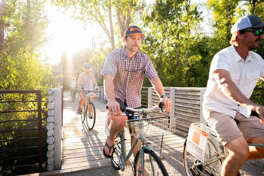 Three people riding bicycles on a wooden bridge surrounded by trees. 3