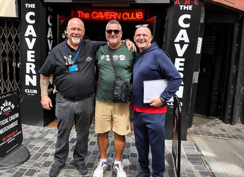 Tre mænd står foran The Cavern Club, en bygning der er sort med hvide bogstaver. 3