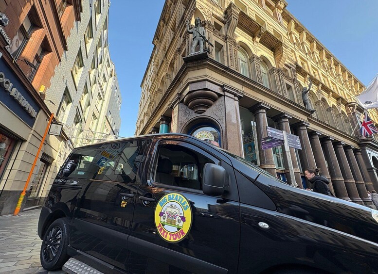 A black taxi with a Big Beatles Taxi Tour logo parked in front of a historic building with ornate architecture. 3
