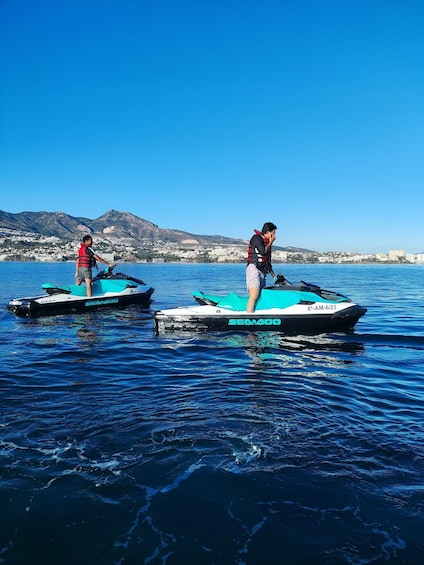 Two people jet-skiing on a clear day with a mountainous landscape in the background. 3