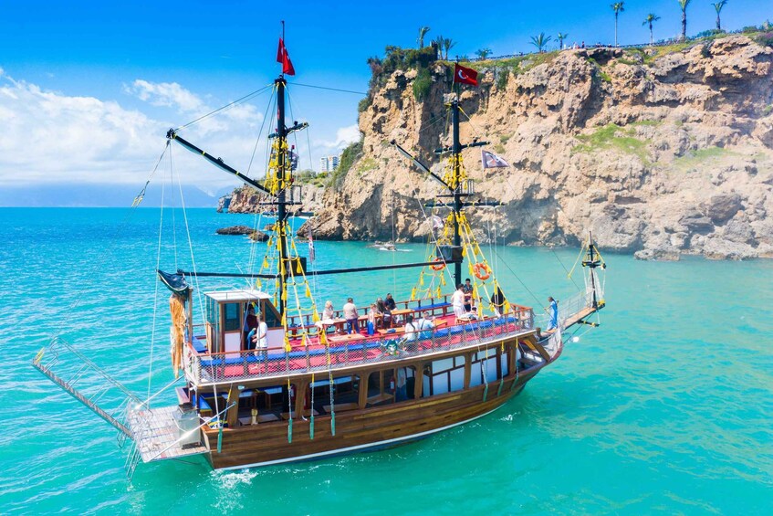 A wooden boat with passengers, anchored near a rocky coastline with palm trees. 4