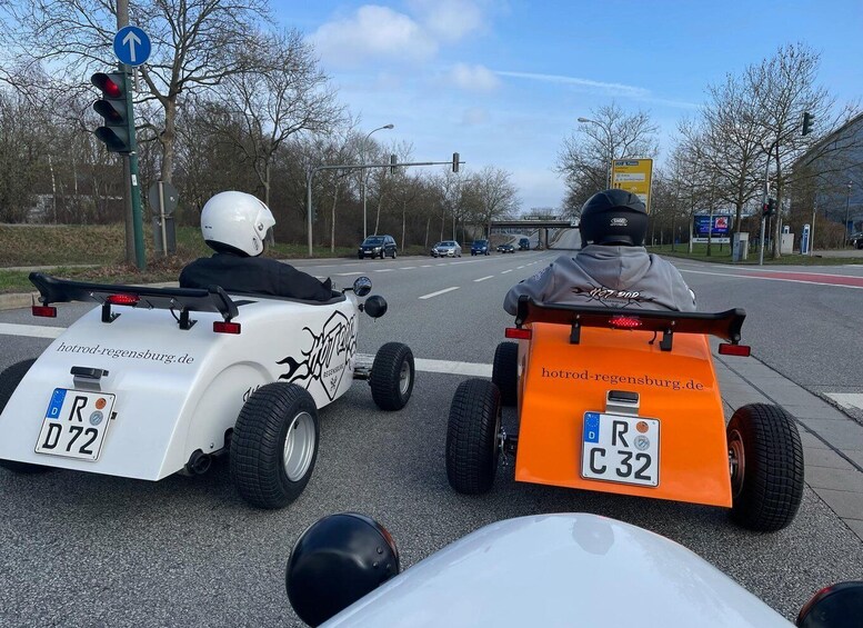 Two go-karts on a road with traffic lights and a directional sign in the background. 5