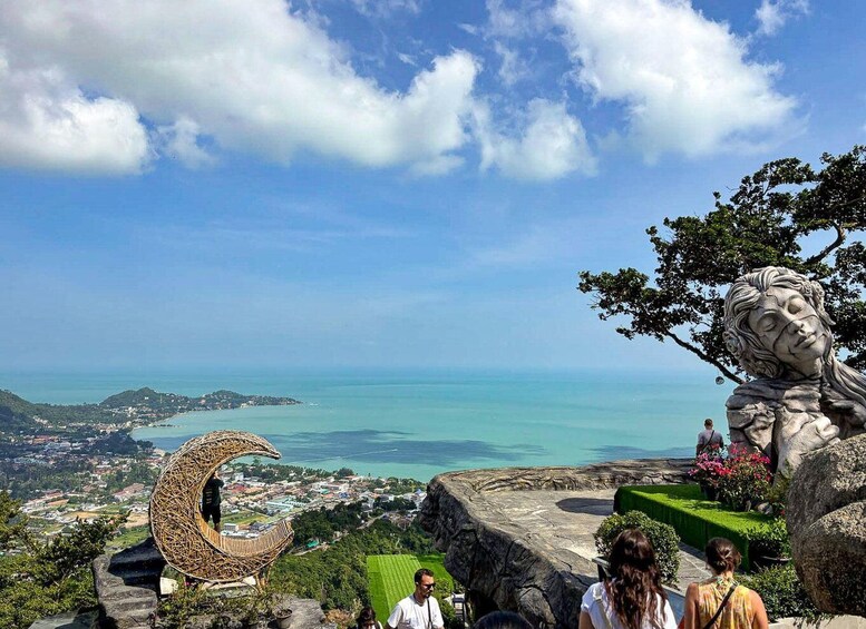 A scenic overlook with a view of the sea, a stone sculpture, and a wicker chair. 5
