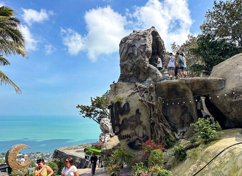 A large rock formation with a carved face, a crescent moon sculpture, and a view of the ocean. 1