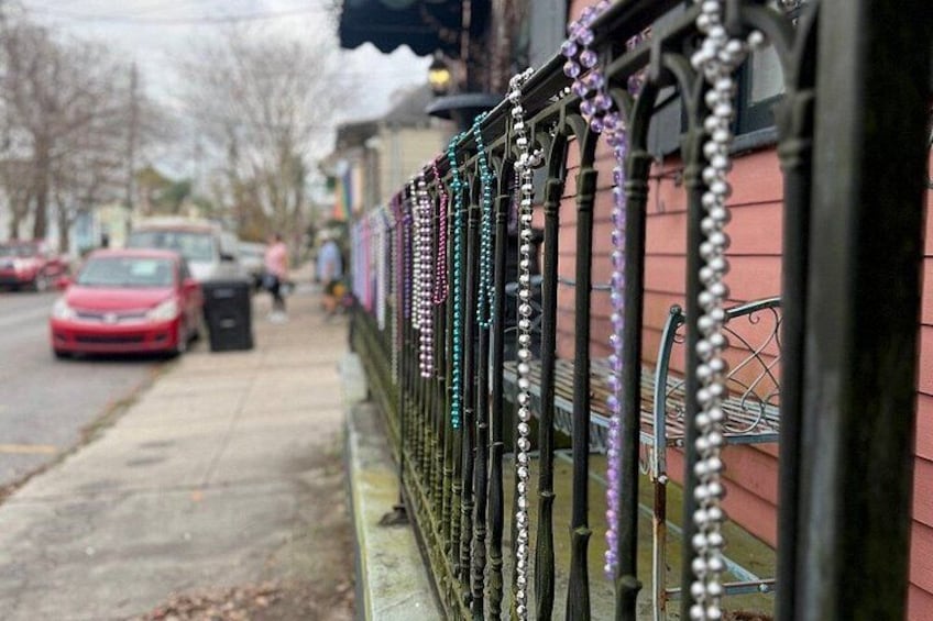 Une rue bordée d’une clôture décorée de perles colorées, une voiture rouge garée sur le côté et, au fond, un bâtiment à la façade rose. 3