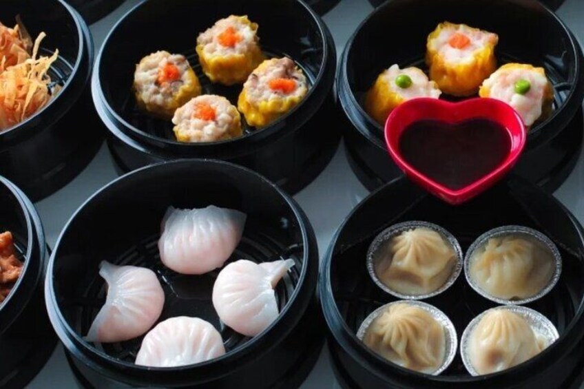 Forskellige dim sum retter i sorte skåle, herunder dumplings og boller, med en rød, hjerteformet skål i midten. 4
