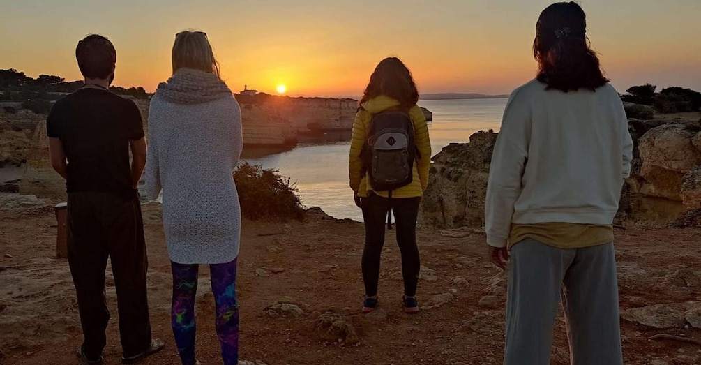 Four people standing on a rocky shore at sunset. 1