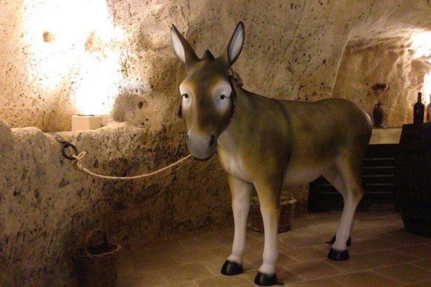 Una estatua de burro en un entorno parecido a una cueva, con paredes de piedra y una fuente de luz. 1