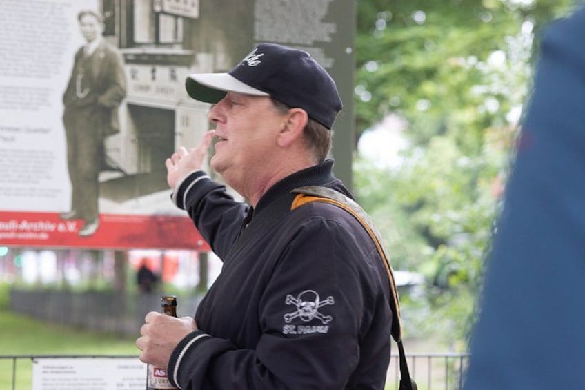 A person wearing a cap and a jacket with a skull and crossbones emblem, holding a bottle. 4