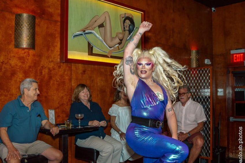 A person in a shiny blue outfit dancing in a room with wooden walls and an exit sign. 2