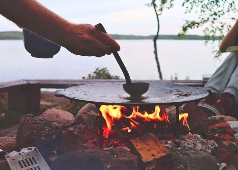 A person cooking over an open flame with a pot on a portable stove. 1
