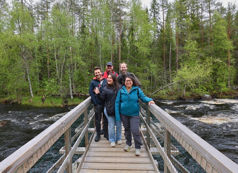 A group of people on a wooden bridge over a river, surrounded by a forest. 4