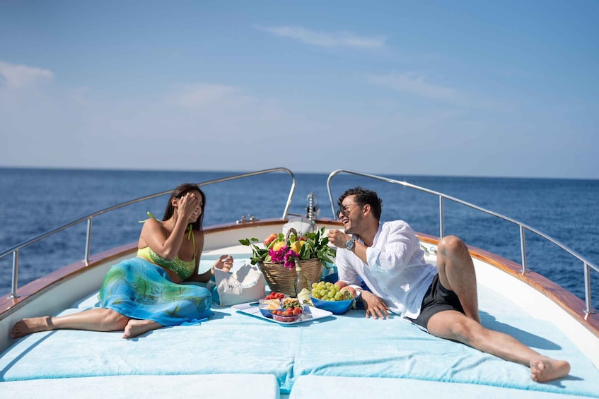 Two people on a boat with a picnic setup including fruits and vegetables. 1