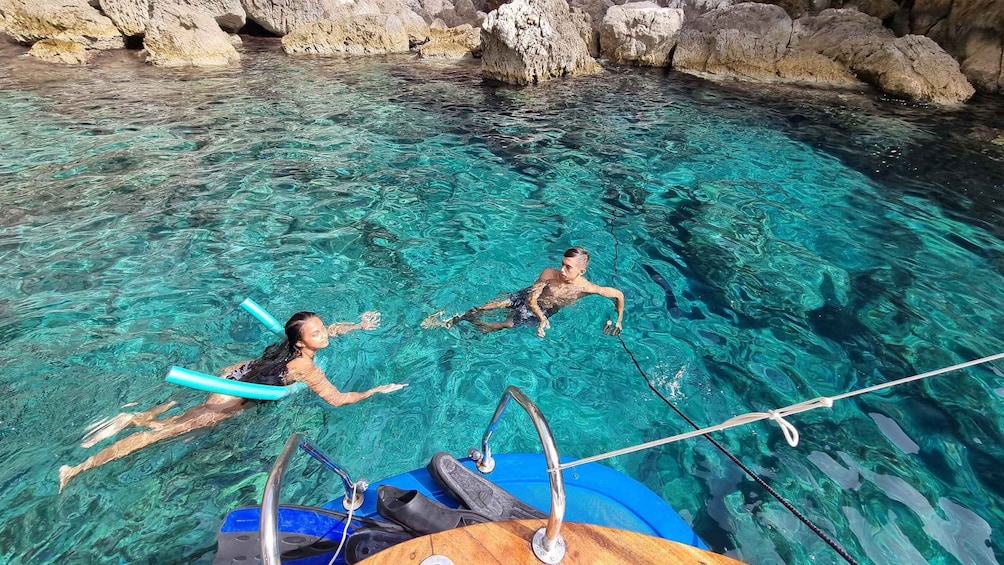 Two people swimming in a clear blue pool with rocky formations in the background. 3