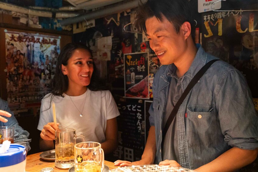 A person in a denim shirt standing at a bar counter with a drink in hand. 1