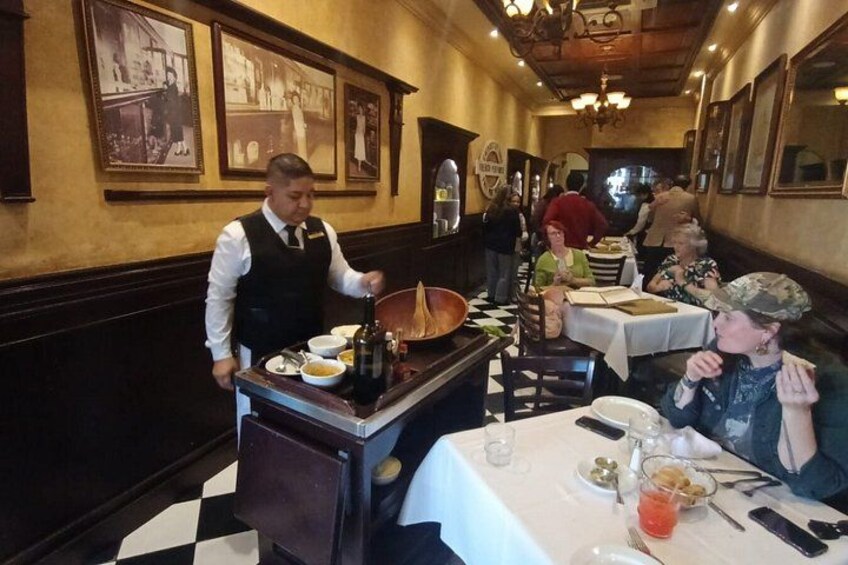L’intérieur d’un restaurant avec des clients, un serveur et un comptoir où sont présentés des plats. 2