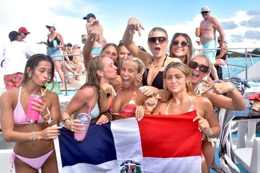 A group of people on a boat, holding a flag, with a body of water and a clear sky in the background. 3