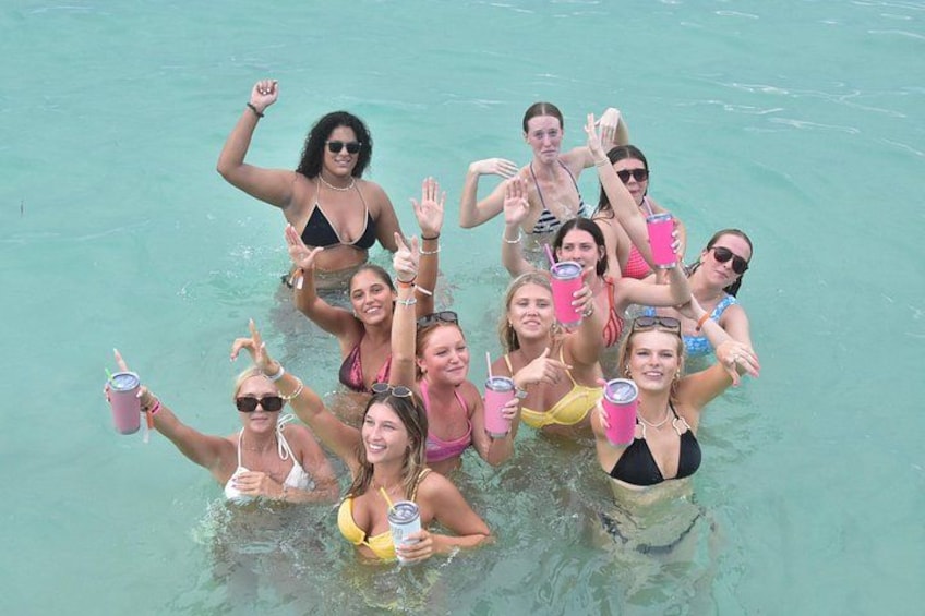 A group of people in a clear blue body of water, some holding drinks. 4