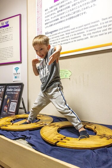 A child standing on a wooden platform with a sign about a ninja museum. 4