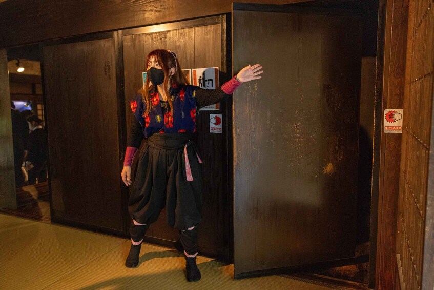 A person in traditional attire standing next to a wooden door with a reflective surface. 5