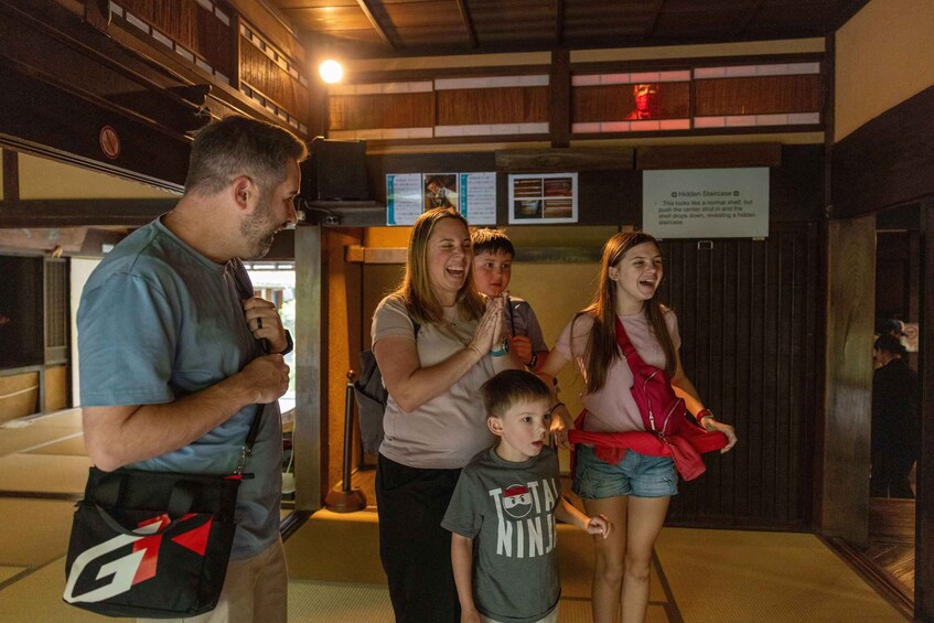 A group of people in an indoor setting with wooden paneling and a sign indicating a hidden staircase. 3