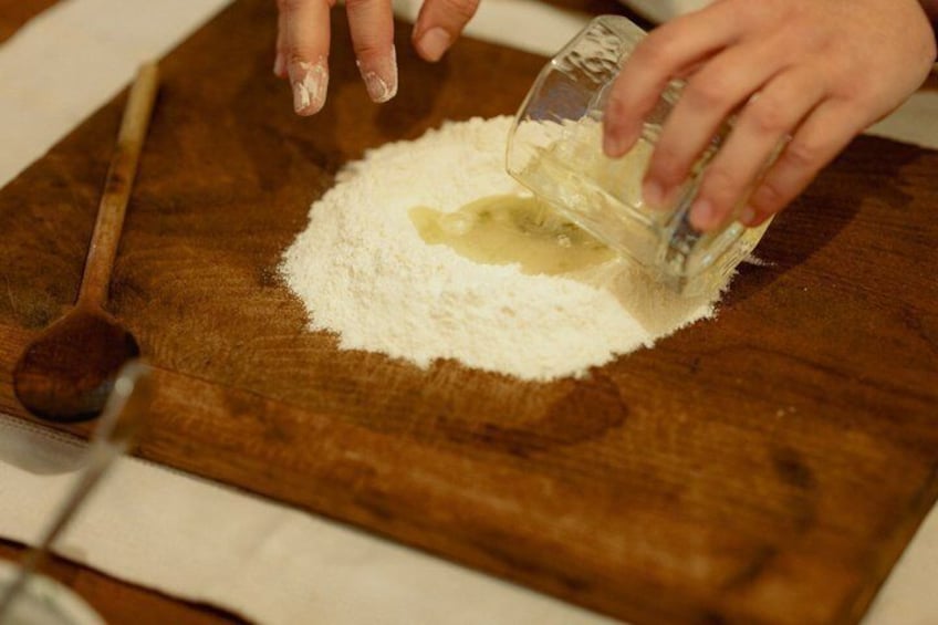 Una persona versa un liquido in una ciotola di farina su un tagliere di legno. 1