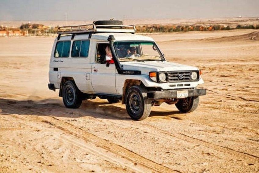 Un véhicule tout-terrain blanc, équipé d’un porte-bagages sur le toit, circulant sur un terrain sablonneux. 1
