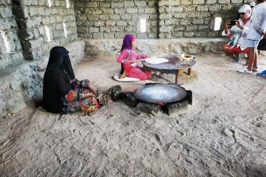 Une scène de cuisine traditionnelle mettant en scène un gros poisson sur une pierre plate, une femme vêtue de rose et une autre vêtue de noir. 5