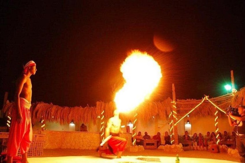 Une représentation de jonglage avec le feu, avec un artiste vêtu de rouge et un autre de blanc, devant un public assis en arrière-plan. 3