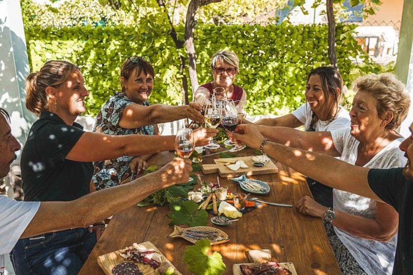 Eine Gruppe von Menschen stoßen mit Weingläsern um einen Holztisch mit Essen und einer Weinflasche an. 2