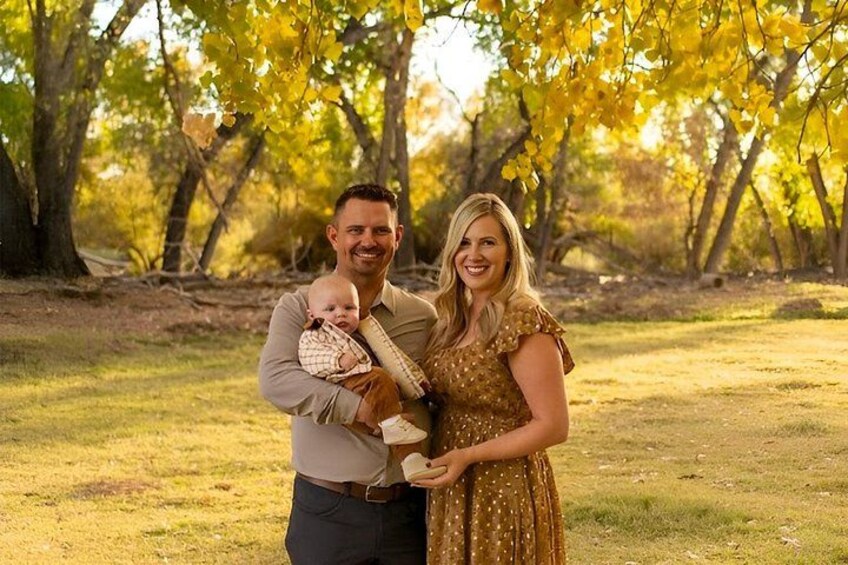 A person holding a baby in a park with trees and grass. 2