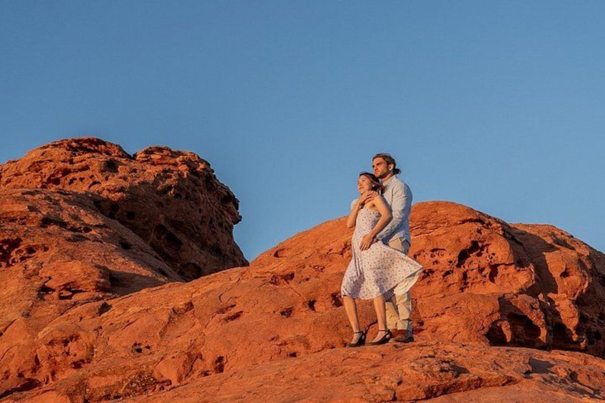 A couple standing on a red rock formation with a clear sky. 1