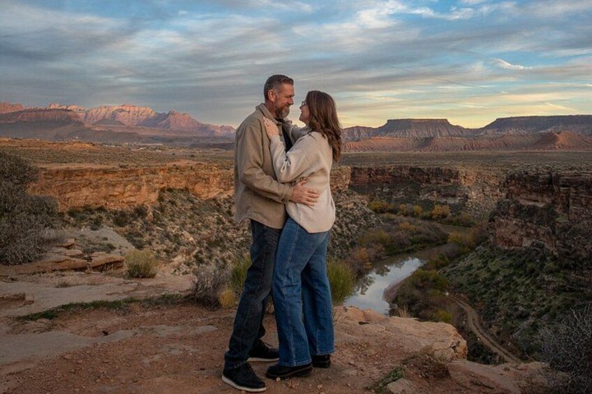 A couple embracing in a desert landscape with a river and mountains in the background. 3