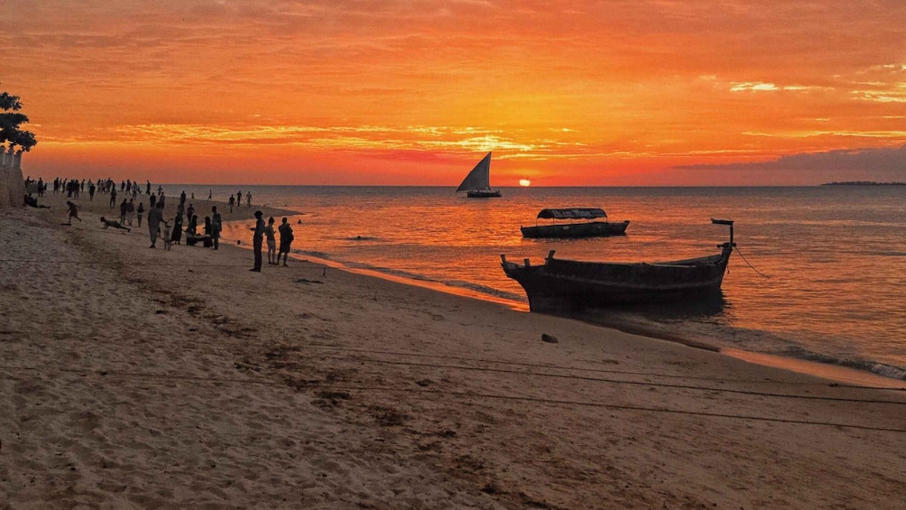 A beach at sunset with people, boats, and palm trees. 2