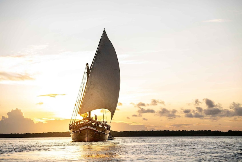 A sailing boat with a large sail on a body of water during sunset. 4