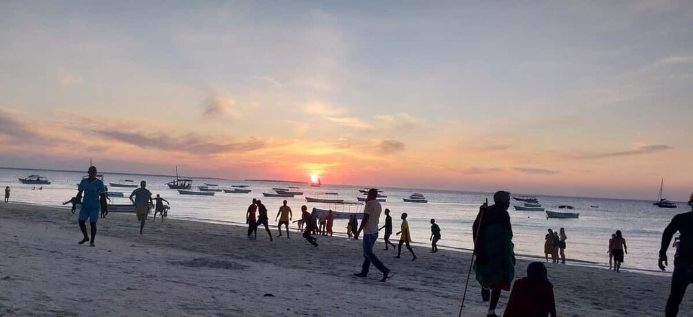 A beach with people walking and boats in the water during sunset. 3